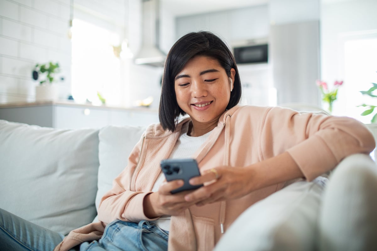 Young woman using a smart phone while sitting on a couch customer review