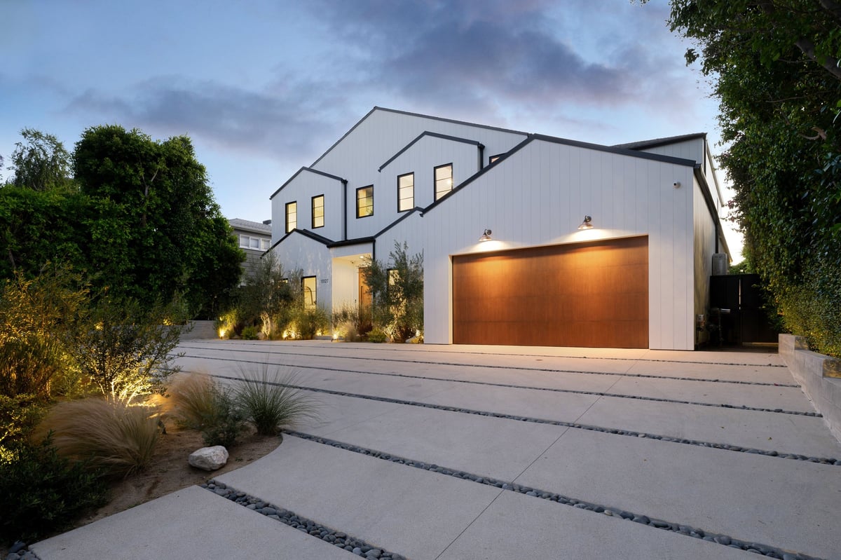 Modern house exterior with wooden garage door and landscaped driveway at dusk