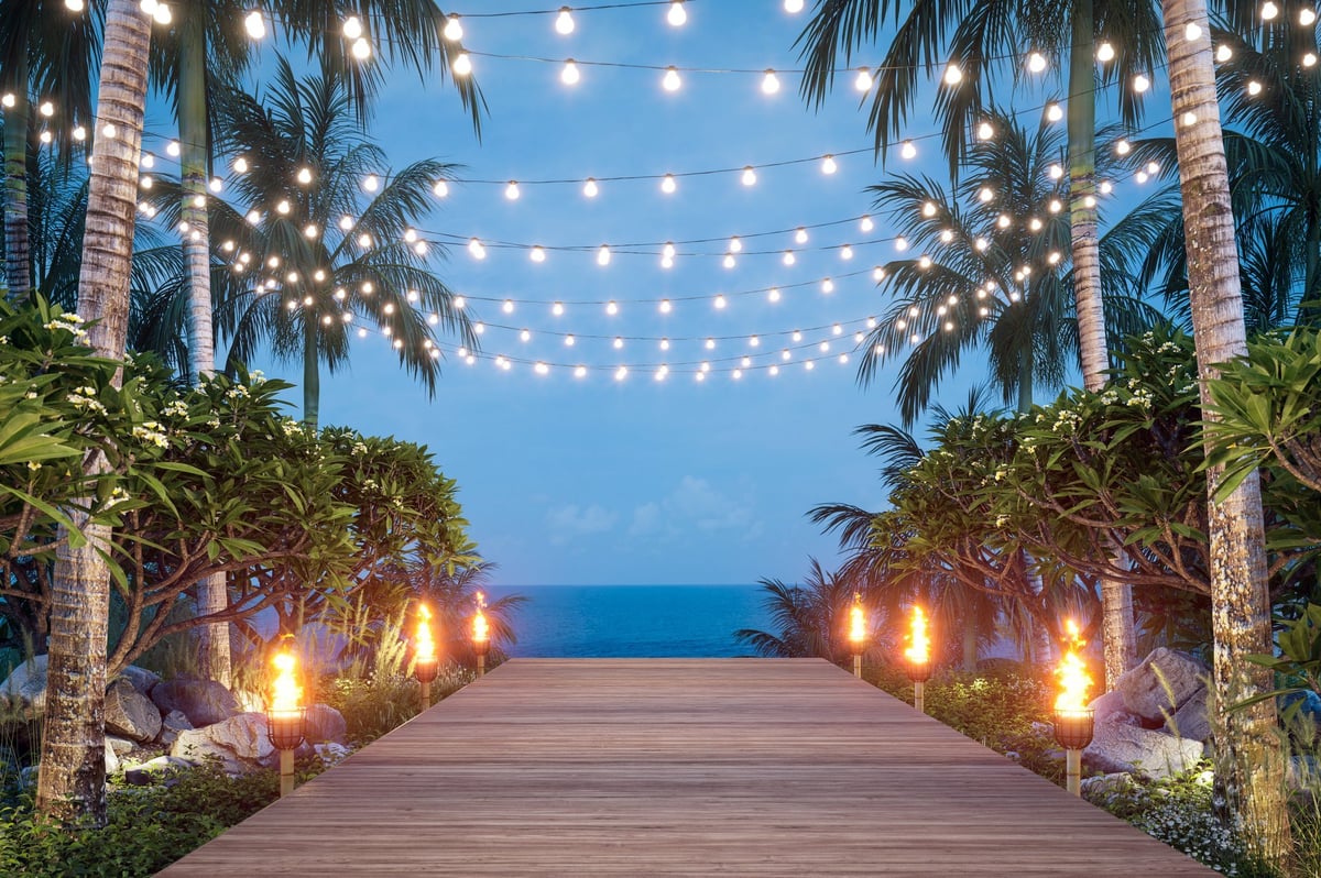 Wooden balcony at dusk with string lights and torches surrounded by tropical plants