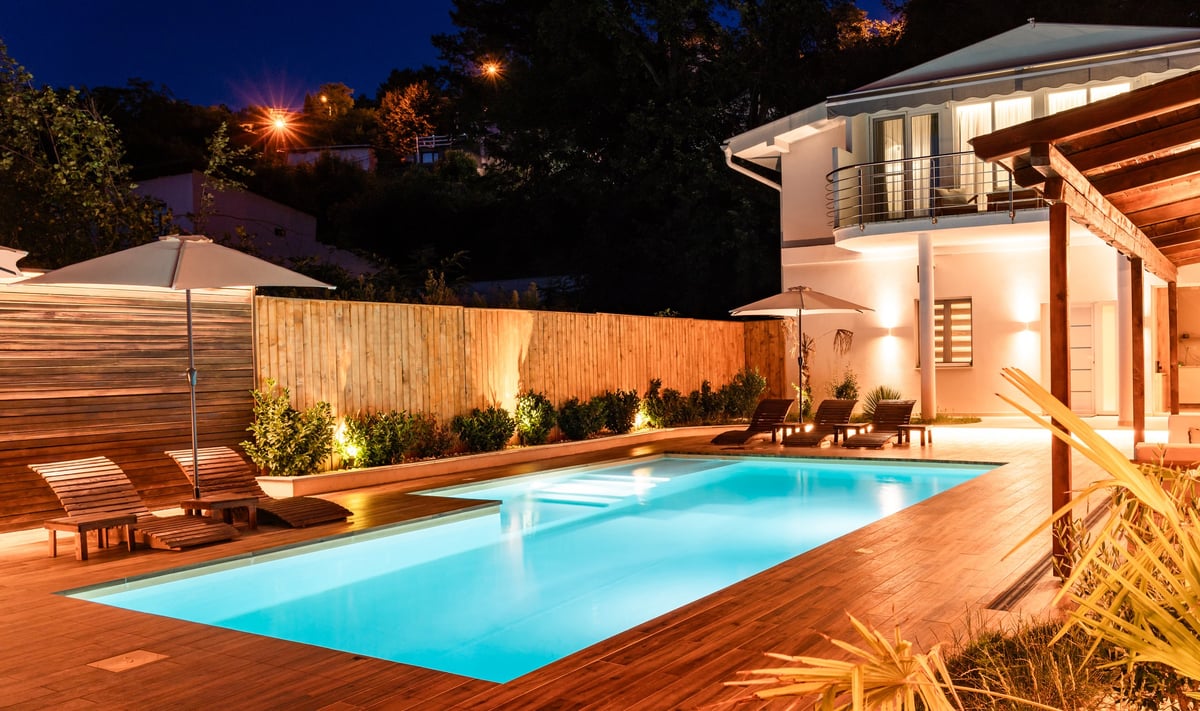 Elegant backyard with illuminated swimming pool and modern house at night with cozy lighting