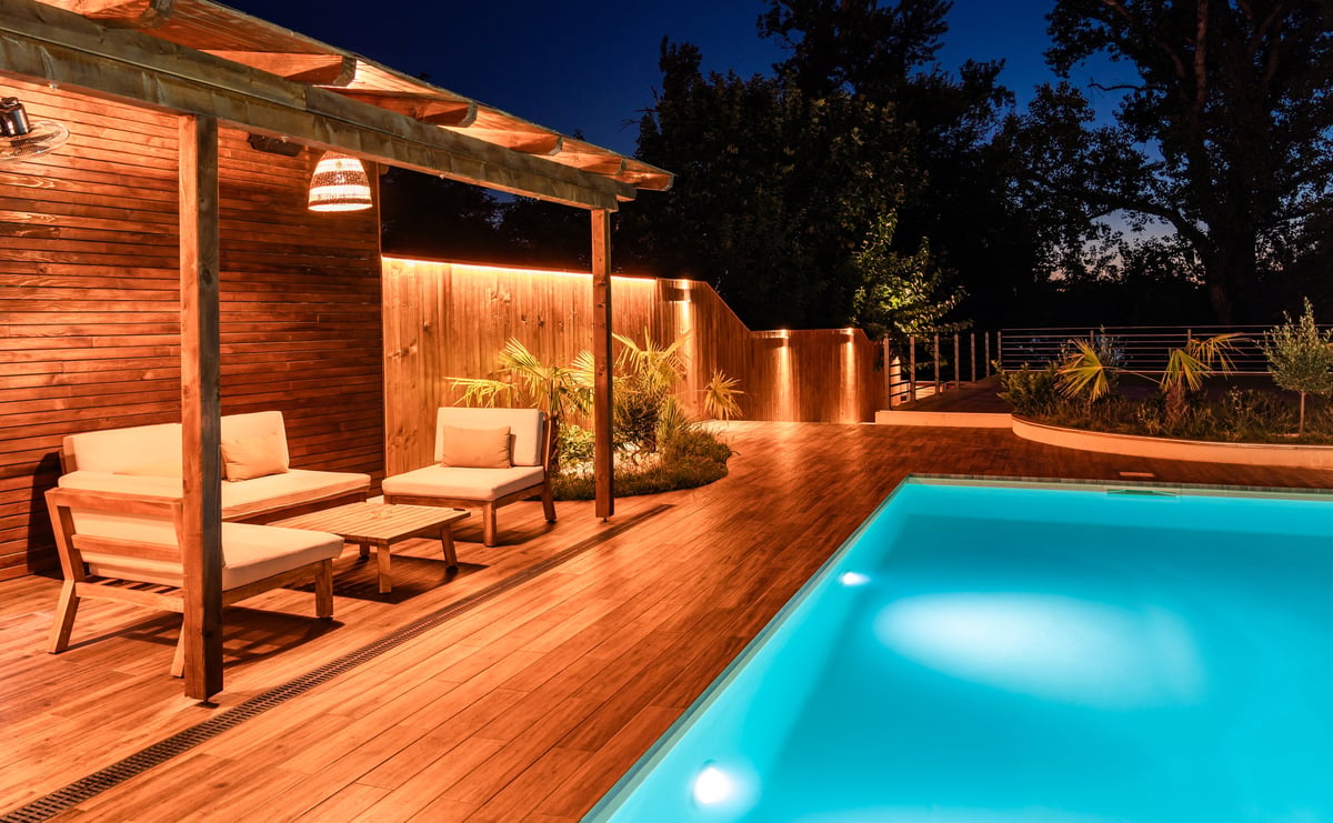 Modern outdoor lounge area with wooden pergola and swimming pool at night