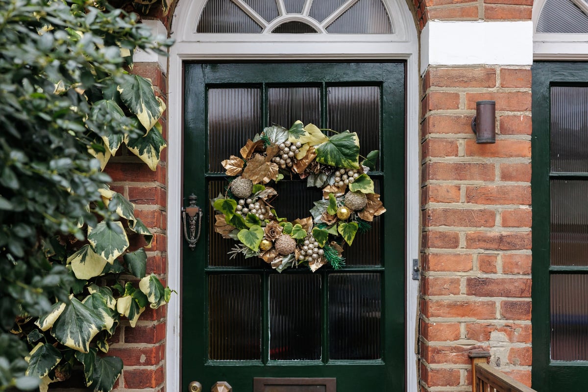 Festive Christmas wreath with gold and green decorations hanging on a green front door