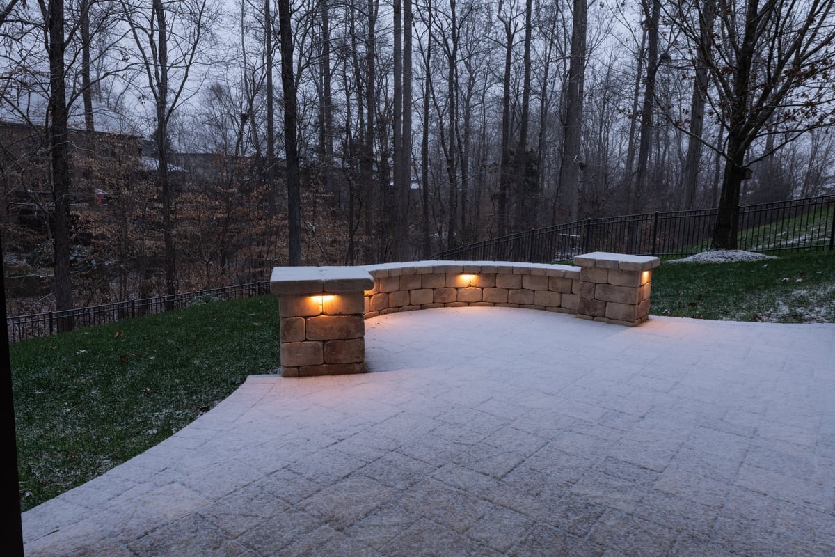 Backyard patio with a curved stone wall illuminated by warm lights