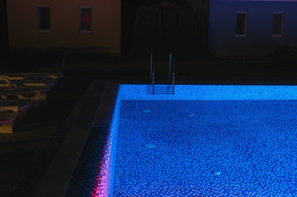 Outdoor summer swimming pool illuminated by vibrant underwater lights at night