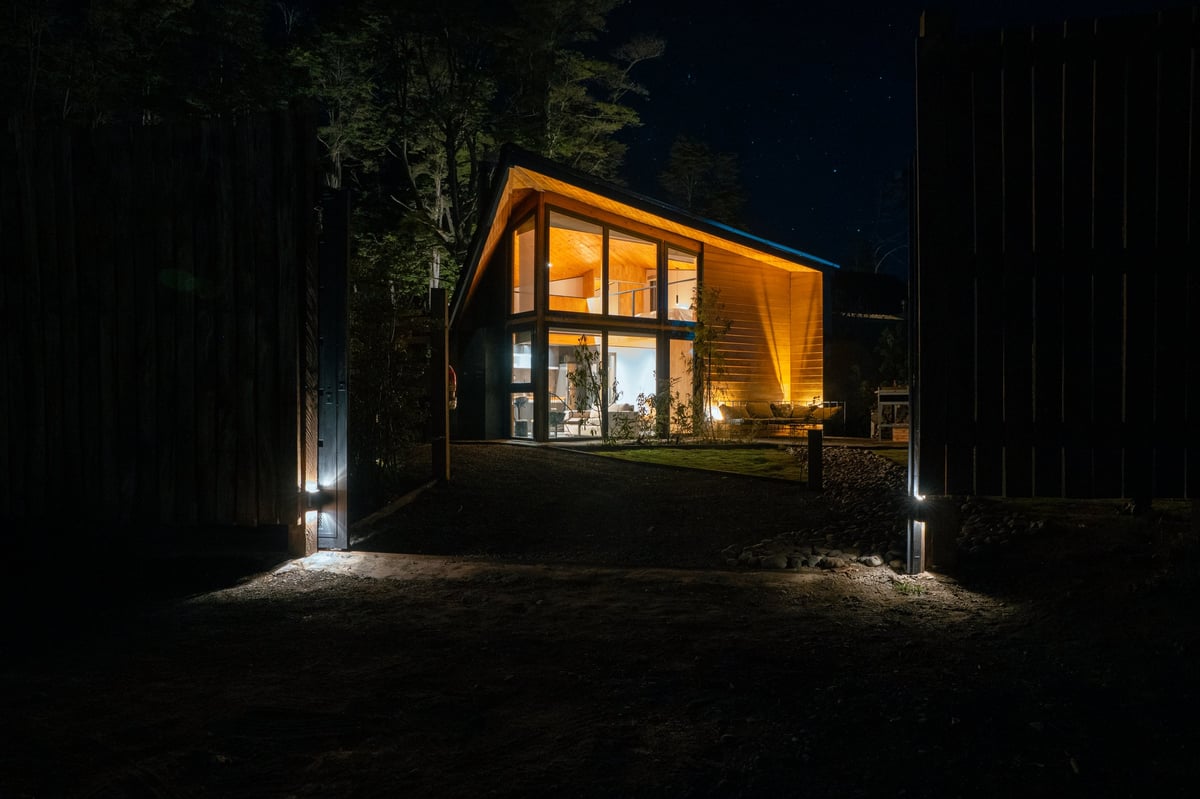 Modern wooden home warmly illuminated at night surrounded by trees in a forest environment