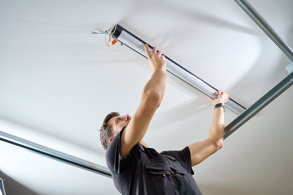 Man in workwear installing a linear LED light fixture on the ceiling indoors