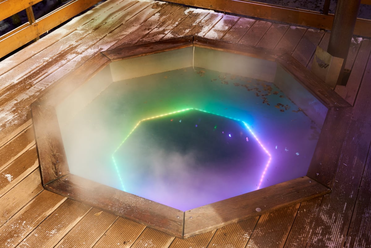 Octagonal wooden hot tub glowing neon with rainbow LED ring reflecting on water