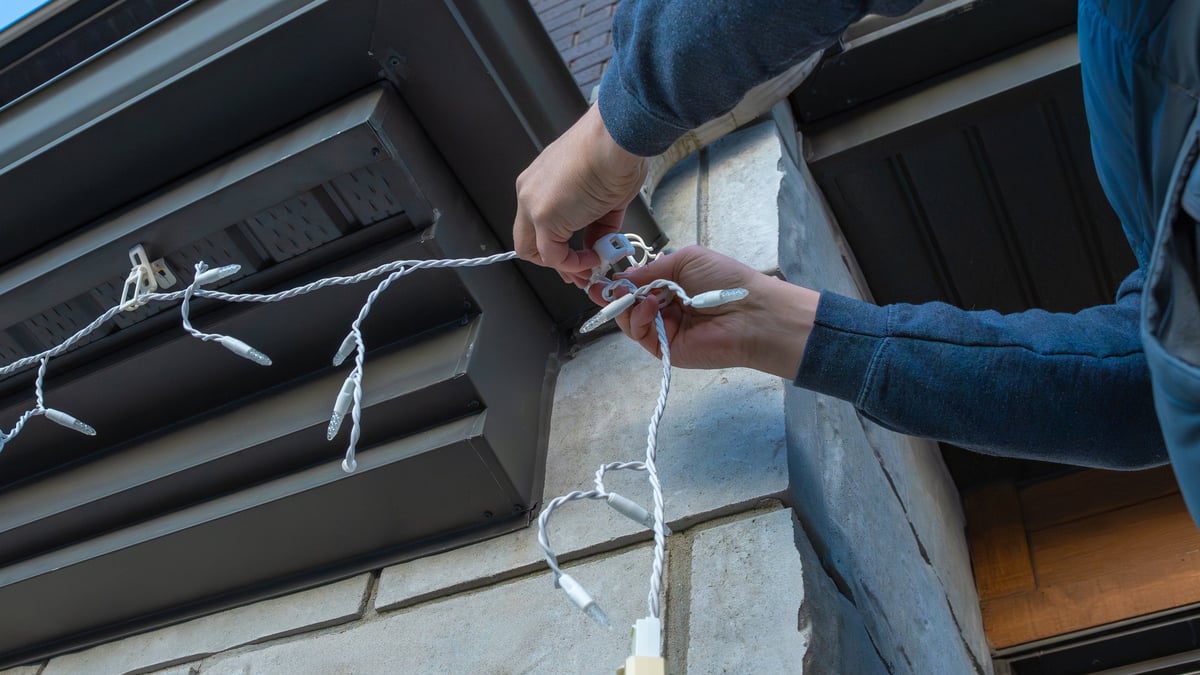 Individual attaching decorative lights to a building exterior for upcoming celebrations