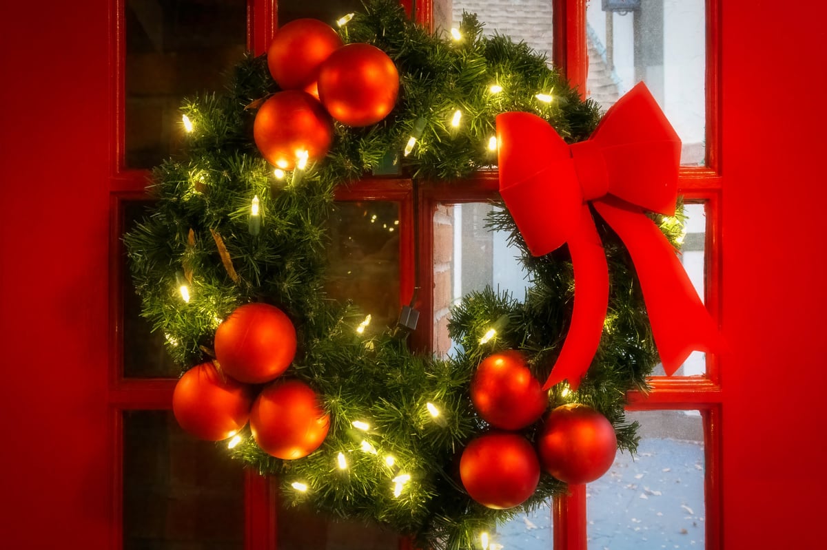A red Christmas wreath hangs from a similarly colored door