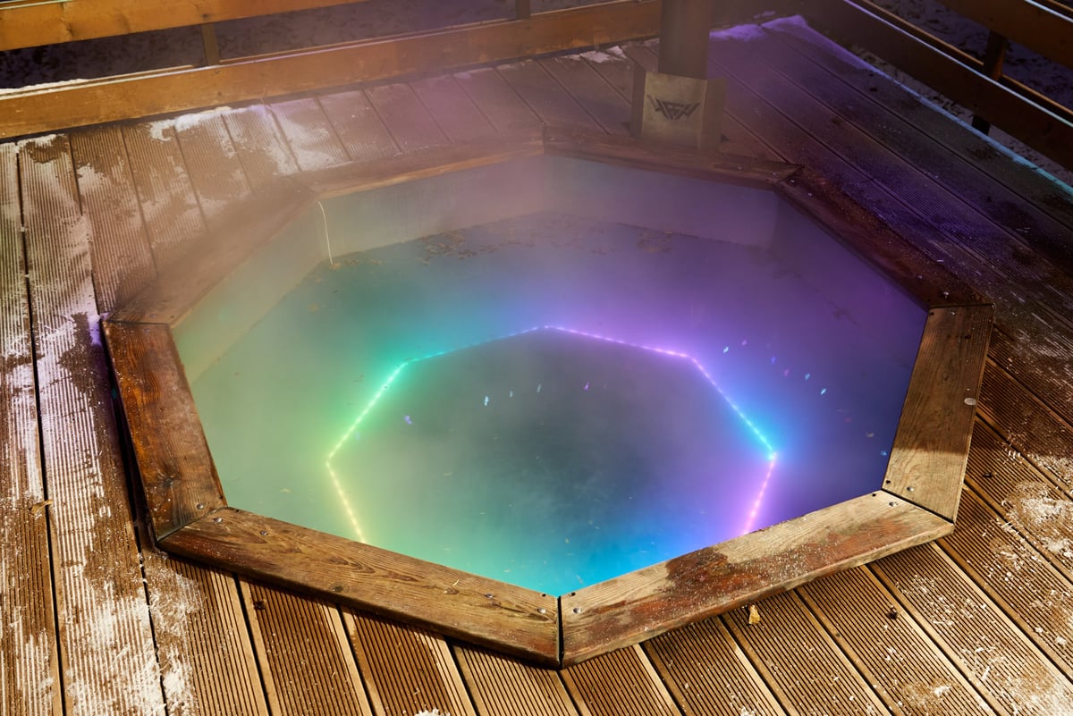 Octagonal outdoor hot tub lit teal and steaming with soft LED halo
