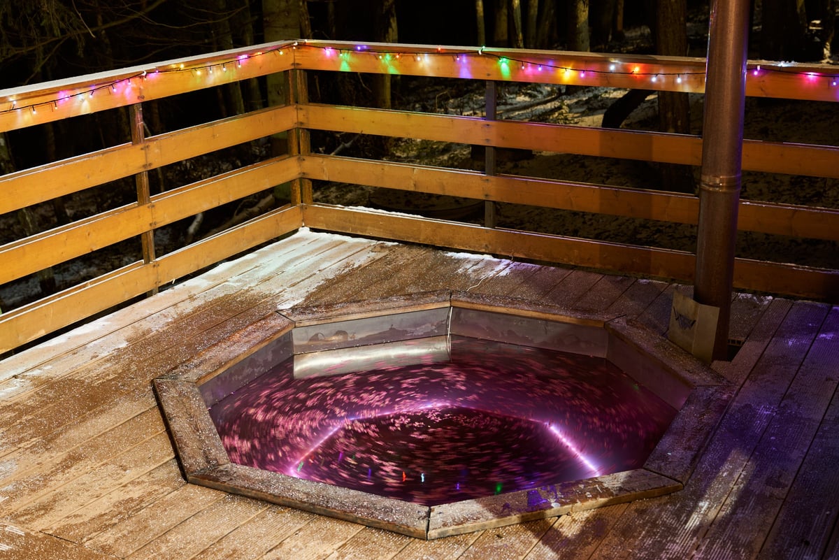 Vibrant octagonal spa with neon underglow and string lights on deck