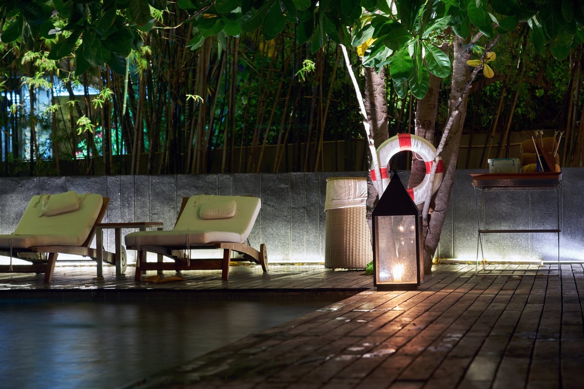 Illuminated swimming pool deck and relaxation area with bamboo trees under evening light