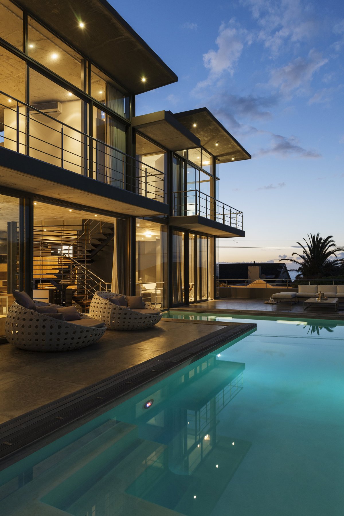 Modern house with large windows and poolside seating at dusk